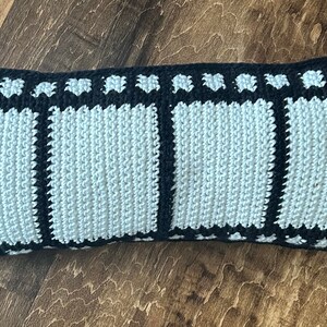 May include: A long, rectangular pillow with a black and white film strip design. The pillow is made of crocheted yarn and has a light blue center.