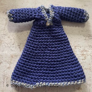 May include: A crocheted doll's dress in a deep blue colour with a white and gold trim. The dress has long sleeves and a V-neck.