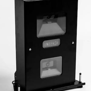 May include: A black rectangular device with two transparent, geometric windows. The word "UNEEKOR" is displayed on the front. The device has a base with two metal posts and a slot on top.
