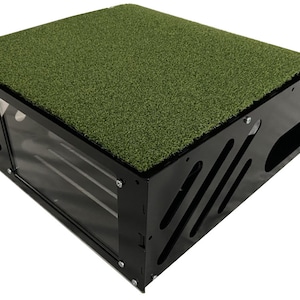 Op de afbeelding: Zwart en groen hondenhuis met een groen kunstgras dak. Het huis heeft een transparant kunststof raam en een zwart metalen frame.
