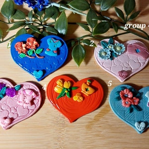 May include: Five heart-shaped resin ornaments with different designs. Each ornament features a different color and design, including flowers, a baby bottle, a nurse's hat, and a pair of shoes. The ornaments are arranged in a row on a wooden surface. The text "group 47" is visible in the top right corner of the image.