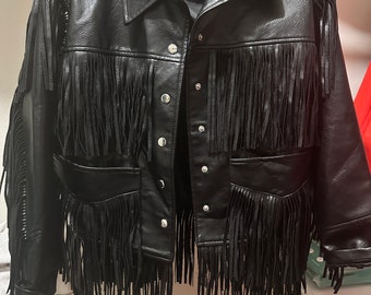 May include: Black faux leather jacket with fringe detailing. The jacket has a button closure and two flap pockets.
