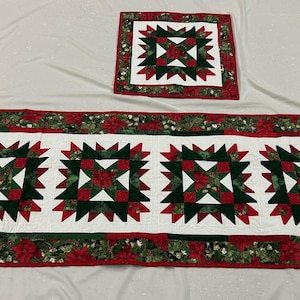 May include: A Christmas-themed table runner and matching placemat. The runner features four large starburst designs in red, green, and white, with a floral border. The placemat mirrors the starburst design.