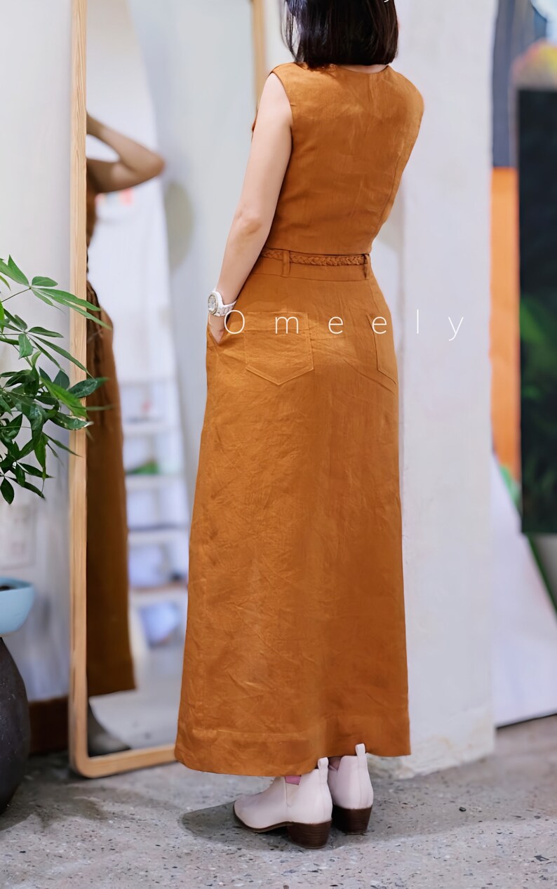 Peut inclure: Un haut sans manches couleur rouille et une jupe longue taille haute assortie avec une fine ceinture tress&eacute;e, deux poches arri&egrave;re et un ourlet droit. Le texte Omeely est visible sur la jupe. L'ensemble est port&eacute; avec des bottines rose clair.