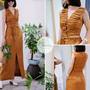Peut inclure: Un ensemble deux pi&egrave;ces de couleur marron chaud compos&eacute; d'un haut court sans manches fronc&eacute; avec un d&eacute;collet&eacute; en V et une fermeture boutonn&eacute;e, associ&eacute; &agrave; une jupe longue taille haute avec une fente avant, une ceinture tress&eacute;e et des poches.