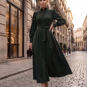 May include: A dark forest green midi dress featuring a high mandarin collar, long sleeves with gathered shoulders, a full button-down front, and a matching fabric tie belt at the waist. The dress has a structured bodice and a flowing skirt.
