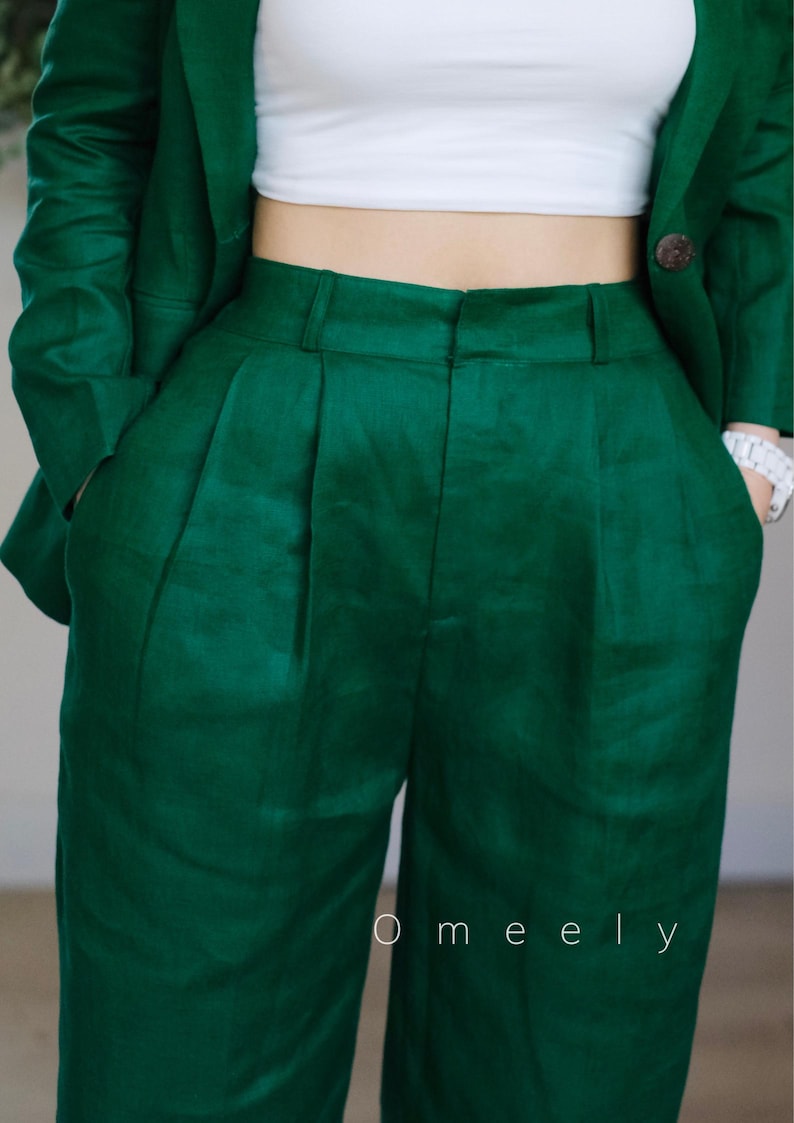 May include: A dark green linen trouser suit with a white top. The trousers have pleats and pockets. The jacket has a button fastening. The text "O meely" is visible on the trousers.