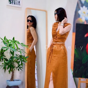 Peut inclure: Un ensemble deux pi&egrave;ces compos&eacute; d'un haut court sans manches, fronc&eacute; et boutonn&eacute;, et d'une jupe longue taille haute assortie de couleur rouille unie. La jupe pr&eacute;sente une fente sur le devant, des poches lat&eacute;rales et une fine ceinture tress&eacute;e.