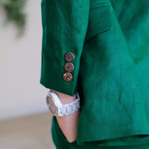May include: A green linen blazer with three brown coconut shell buttons on the sleeve.