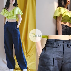 May include: A woman is wearing a lime green ruffled crop top and dark blue wide-leg pants with a high waist. The pants have a button closure and a belt loop. The woman is standing in front of a yellow wall.