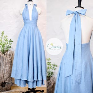 May include: A light blue halter dress with a flowing skirt, displayed on a mannequin. The dress features a deep V-neckline and a bow detail at the back. The dress is floor-length and has a layered skirt. The dress is made of a soft fabric.