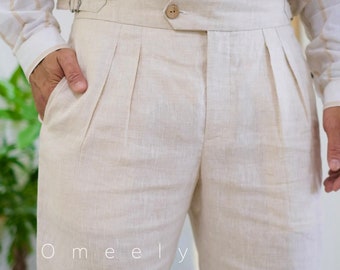 May include: Beige trousers featuring a high-waisted design with double pleats, a central button closure, and side adjusters with metal buckles. The trousers are paired with a long-sleeved shirt featuring vertical beige stripes and brown buttons.