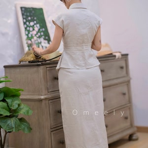 May include: A two-piece set consisting of a short-sleeved, collared peplum top and a matching floor-length skirt in a solid off-white color. The top features a cinched waist with a wide band, and the skirt has a straight, clean-lined silhouette.