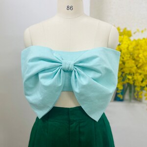 May include: A light blue strapless top with a large bow in the front. The top is on a white mannequin and the mannequin is wearing green pants.