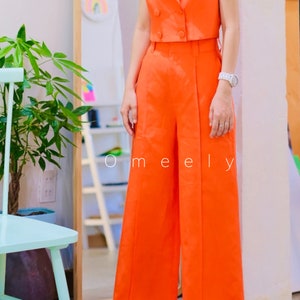 K&ouml;nnte beinhalten: Ein leuchtend orangefarbener &auml;rmelloser Blazer mit doppelreihigem Verschluss und dazu passende weite Hosen. Das Outfit wird mit wei&szlig;en Schuhen und Sonnenbrillen gestylt.