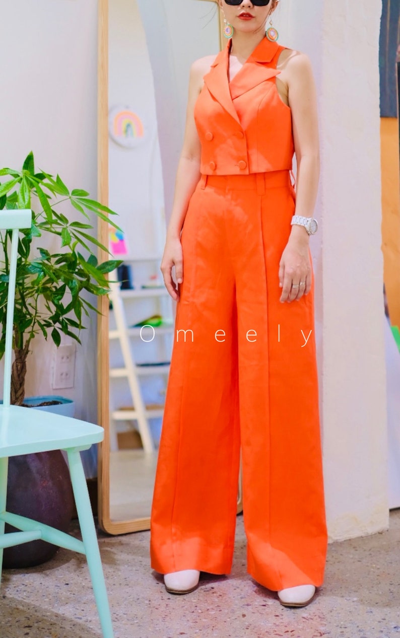 K&ouml;nnte beinhalten: Ein leuchtend orangefarbener &auml;rmelloser Blazer mit doppelreihigem Verschluss und dazu passende weite Hosen. Das Outfit wird mit wei&szlig;en Schuhen und Sonnenbrillen gestylt.