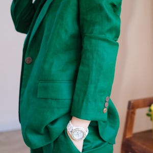 May include: A green linen blazer and matching trousers with a white watch on the left wrist.