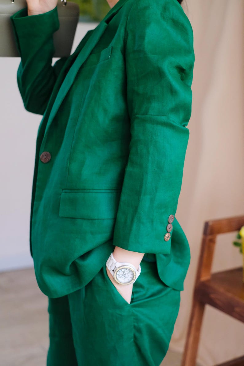 May include: A green linen blazer and matching trousers with a white watch on the left wrist.