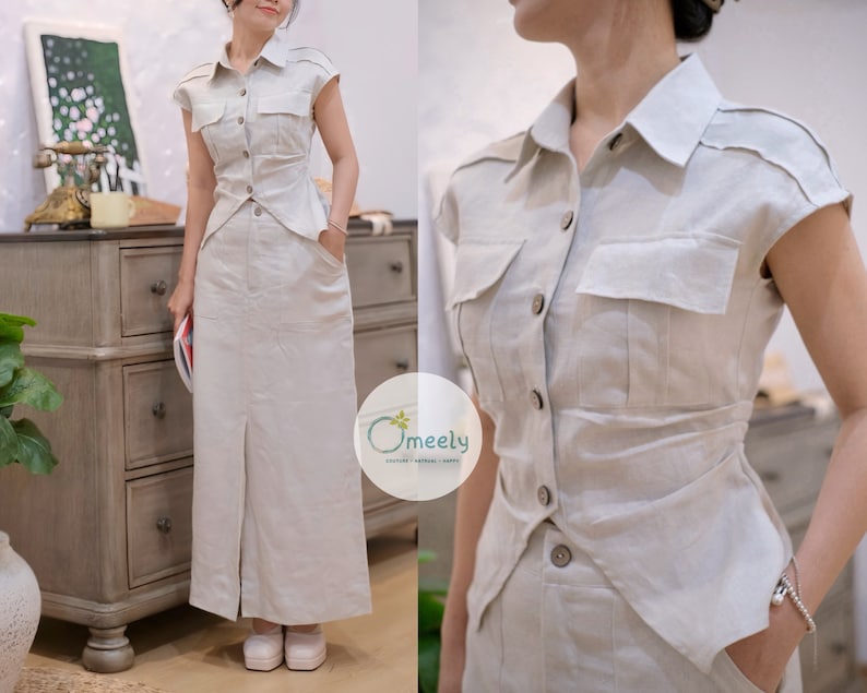 May include: A beige two-piece set consisting of a short-sleeved button-down shirt with two chest pockets and a matching floor-length skirt with a front slit and side pockets. The shirt features a pointed collar and a tapered waistline design.