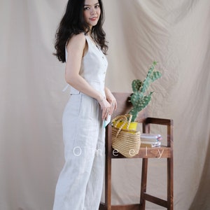Puede incluir: Un chaleco sin mangas de color beige claro con botones en la parte delantera y pantalones anchos a juego. El conjunto se combina con zapatos blancos. El texto Omeely es visible en letras blancas en la parte inferior de la imagen.