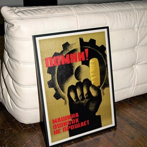 Pu&ograve; includere: Un poster incorniciato con la sagoma nera di un pugno rivolto verso l'alto contro un grande ingranaggio e una forma gialla. Il testo "ПОМНИ!" &egrave; in rosso in alto e "МАШИНА ОШИБОК НЕ ПРОЩАЕТ" in rosso in basso su uno sfondo dorato testurizzato.
