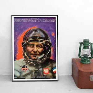 Puede incluir: Un póster vintage con el retrato de un astronauta polaco con un traje espacial. El póster se titula "Pierwszy Polak w Kosmosie", que se traduce como "Primer polaco en el espacio". El astronauta lleva un casco y tiene una expresión seria en su rostro. El póster está sobre un fondo morado y naranja con estrellas.