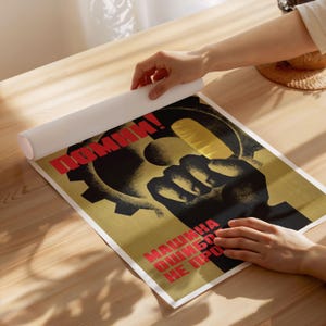 Pu&ograve; includere: Un poster rettangolare con un'illustrazione grafica di un pugno nero che afferra un ingranaggio su sfondo dorato. Il testo in cirillico rosso recita "ПОМНИ!" in alto e "МАШИНА ОШИБОК НЕ ПРОЩАЕТ" in basso. Il poster &egrave; stampato su carta bianca.