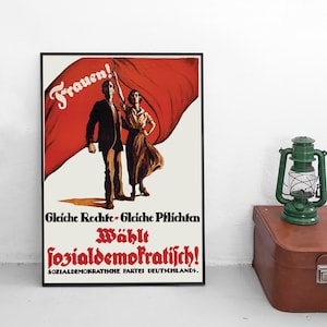 Op de afbeelding: Een ingelijste politieke poster met een man en een persoon voor een grote rode vlag. De tekst luidt: "Frauen!", "Gleiche Rechte - Gleiche Pflichten", "Wählt sozialdemokratisch!" en "SOZIALDEMOKRATISCHE PARTEI DEUTSCHLANDS."