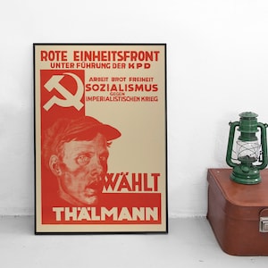 Könnte beinhalten: Ein rotes und weißes Plakat mit dem Text "Rote Einheitsfront Unter Führung der KPD" und "Arbeit Brot Freiheit Sozialismus Gegen Imperialistischen Krieg" und "Wählt Thalmann". Das Plakat zeigt ein rotes Hammer-und-Sichel-Symbol und eine Zeichnung eines Männergesichts.