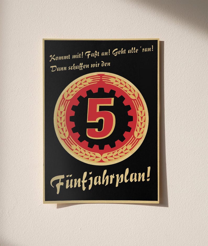 K&ouml;nnte beinhalten: Ein rechteckiges Plakat mit schwarzem Hintergrund, das in der Mitte ein rotes Zahnradsymbol mit einer gro&szlig;en Ziffer 5 zeigt, umgeben von einem goldenen &Auml;hrenkranz. Der Text lautet: Kommt mit! Fa&szlig;t an! Geht alle 'ran! Dann schaffen wir den F&uuml;nfjahrplan!