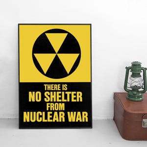Pode incluir: Um poster emoldurado com uma borda preta apresenta um símbolo nuclear amarelo e preto e o texto "THERE IS NO SHELTER FROM NUCLEAR WAR". Uma lanterna verde está em uma mala marrom.