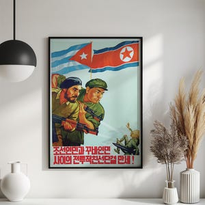 K&ouml;nnte beinhalten: Ein gerahmtes Propagandaposter mit zwei Soldaten in gr&uuml;nen Uniformen, die Gewehre halten, vor dem Hintergrund der Flaggen von Kuba und Nordkorea. Eine kleine Figur st&uuml;rzt im unteren Bereich. Der Text lautet: 조선인민과 꾸바인민 사이의 전투적친선단결 만세!