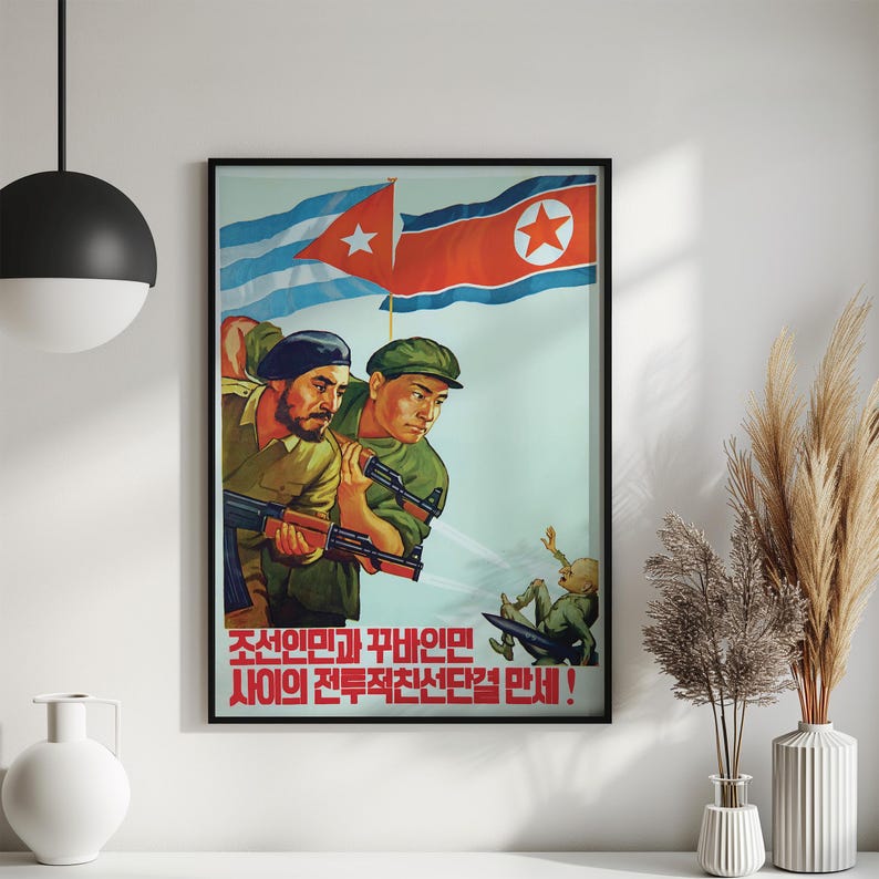 K&ouml;nnte beinhalten: Ein gerahmtes Propagandaposter mit zwei Soldaten in gr&uuml;nen Uniformen, die Gewehre halten, vor dem Hintergrund der Flaggen von Kuba und Nordkorea. Eine kleine Figur st&uuml;rzt im unteren Bereich. Der Text lautet: 조선인민과 꾸바인민 사이의 전투적친선단결 만세!