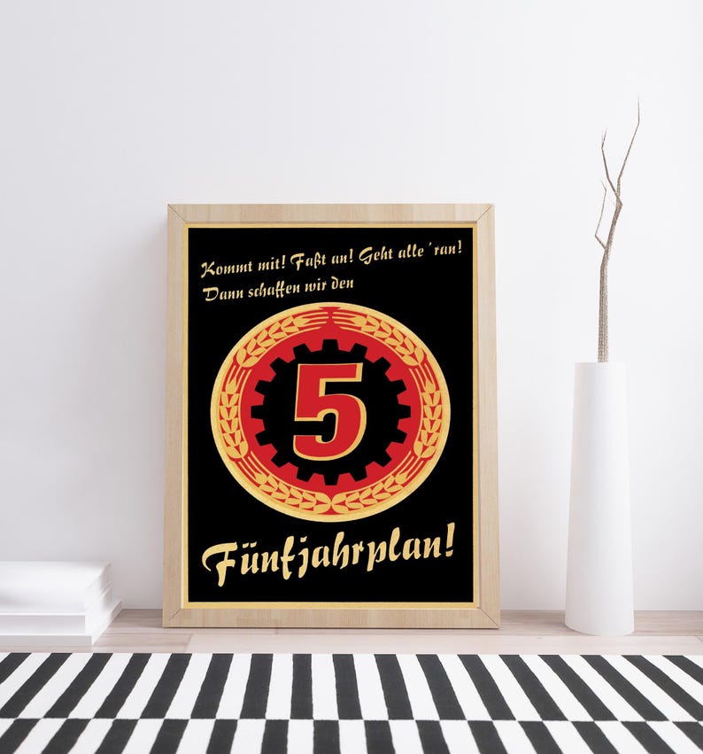 K&ouml;nnte beinhalten: Ein gerahmtes Poster mit schwarzem Hintergrund und einem zentralen roten Zahnrad-Symbol, das die Zahl 5 enth&auml;lt, umgeben von einem goldenen Weizenkranz. Der Text lautet: Kommt mit! Fa&szlig;t an! Geht alle 'ran! Dann schaffen wir den F&uuml;nfjahrplan! in Gold.