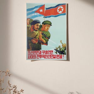 K&ouml;nnte beinhalten: Ein Propagandaposter mit zwei Soldaten in gr&uuml;nen Uniformen, die Gewehre halten und unter den Flaggen von Kuba und Nordkorea stehen. Eine kleine Figur ist darunter fallend dargestellt. Roter koreanischer Text steht am unteren Rand des Posters.