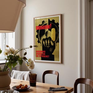 Pu&ograve; includere: Un poster incorniciato raffigurante la sagoma nera di un pugno alzato su uno sfondo giallo con una forma di ingranaggio nero. Il testo in rosso recita "ПОМНИ!" in alto e "МАШИНА ОШИБОК НЕ ПРОЩАЕТ" in basso. Il poster &egrave; appeso a una parete chiara.