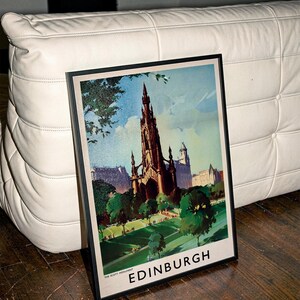 May include: A framed travel poster featuring a dark, detailed illustration of the Scott Monument in Edinburgh, Scotland. The artwork displays a green park in the foreground, blue sky, and the text THE SCOTT MONUMENT and EDINBURGH at the bottom.