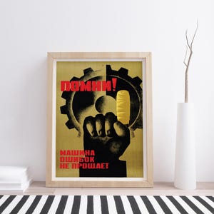 Pu&ograve; includere: Un poster incorniciato raffigurante la sagoma nera di un pugno che tiene un ghiacciolo giallo davanti a un grande ingranaggio nero. Il testo in rosso recita "ПОМНИ!" in alto e "МАШИНА ОШИБОК НЕ ПРОЩАЕТ" in basso, su uno sfondo giallo tenue.