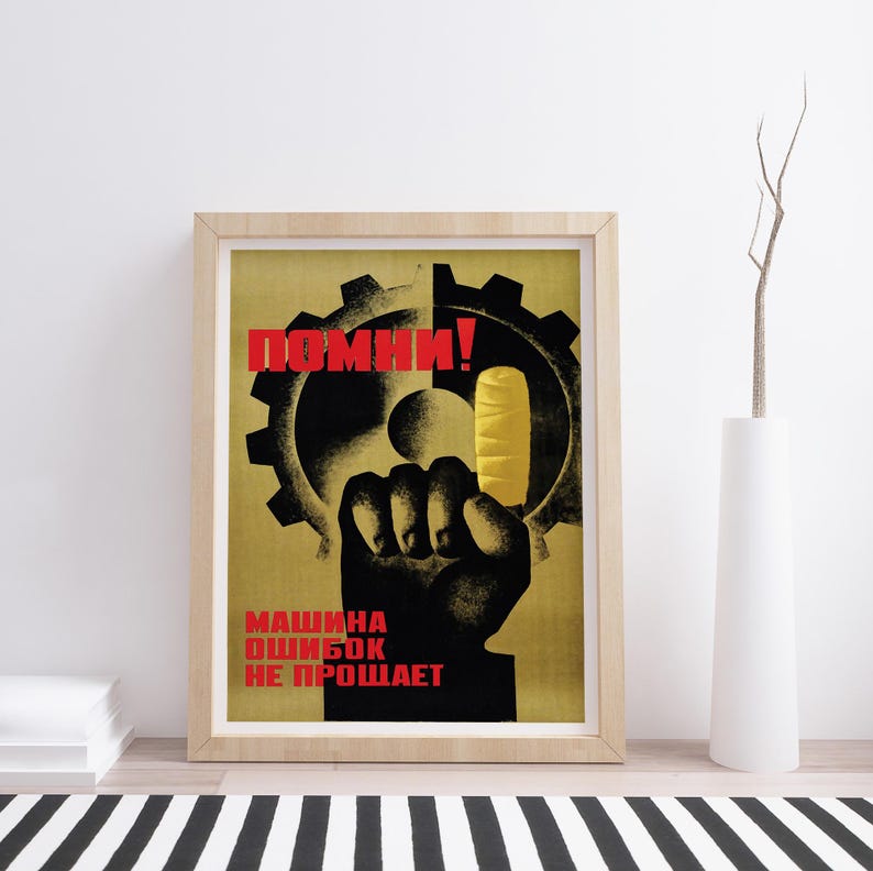Pu&ograve; includere: Un poster incorniciato raffigurante la sagoma nera di un pugno che tiene un ghiacciolo giallo davanti a un grande ingranaggio nero. Il testo in rosso recita "ПОМНИ!" in alto e "МАШИНА ОШИБОК НЕ ПРОЩАЕТ" in basso, su uno sfondo giallo tenue.