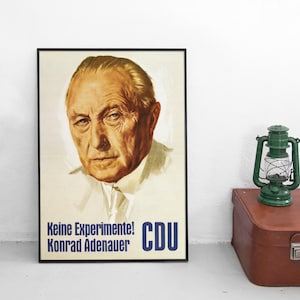 May include: A framed political poster featuring a portrait of Konrad Adenauer with a cream background. The text at the bottom reads "Keine Experimente!" and "Konrad Adenauer" in black, with "CDU" in large blue letters on the right side.