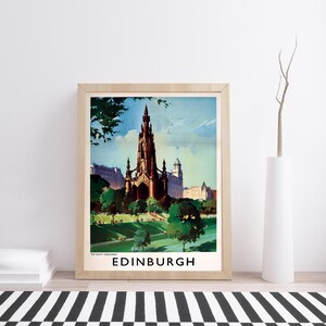 May include: A framed travel poster print featuring a vintage-style illustration of the Scott Monument in Edinburgh, Scotland. The artwork displays the dark gothic spire surrounded by green trees and a park, with the text THE SCOTT MONUMENT EDINBURGH.