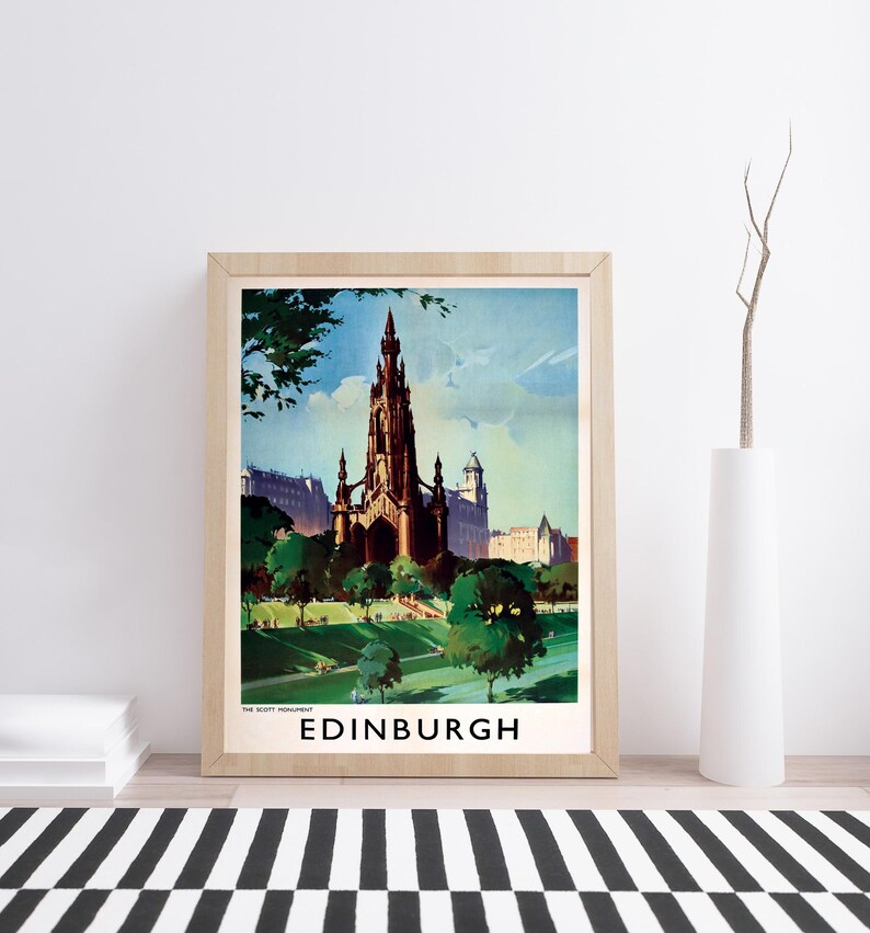 May include: A framed travel poster print featuring a vintage-style illustration of the Scott Monument in Edinburgh, Scotland. The artwork displays the dark gothic spire surrounded by green trees and a park, with the text THE SCOTT MONUMENT EDINBURGH.