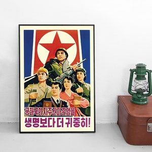 Könnte beinhalten: Ein gerahmtes Propagandaposter mit einer Gruppe von fünf Personen in militärischer und ziviler Kleidung vor einem roten Stern und blauem Hintergrund. Das Poster enthält koreanischen Text in Violett und Rot sowie eine grüne Laterne daneben.