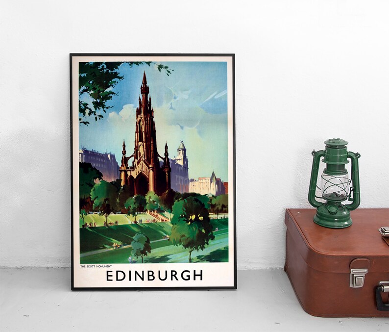 May include: A framed travel poster featuring an illustration of the Scott Monument in Edinburgh, Scotland. The artwork displays the dark gothic spire rising above green parkland and trees under a blue sky. The text reads THE SCOTT MONUMENT EDINBURGH.