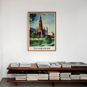 May include: A framed vintage-style travel poster of the Scott Monument in Edinburgh, Scotland, featuring a dark gothic spire against a blue sky, green trees, and grass. The word EDINBURGH is printed in bold black capital letters at the bottom.