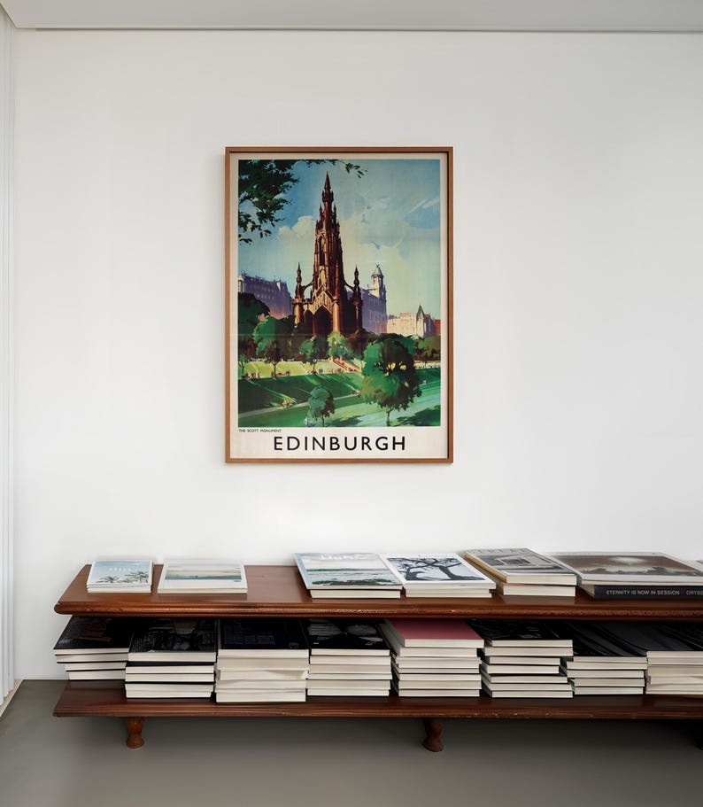 May include: A framed vintage-style travel poster of the Scott Monument in Edinburgh, Scotland, featuring a dark gothic spire against a blue sky, green trees, and grass. The word EDINBURGH is printed in bold black capital letters at the bottom.
