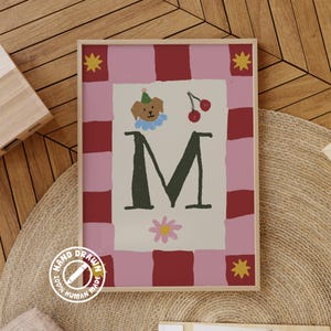 Puede incluir: Una impresión artística enmarcada con un diseño caprichoso. La obra de arte incluye una gran letra "M" en verde oscuro, un perro de dibujos animados con un gorro de fiesta, cerezas y una flor. El fondo tiene un patrón de cuadros rosas y rojos con acentos de estrellas amarillas. La impresión está etiquetada como "Hand Drawn 100% Human Made."