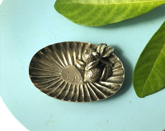 May include: A silver dish with a scalloped edge and a raised design of three limes with leaves. The dish is marked "Ay-Oo" and "Italy".