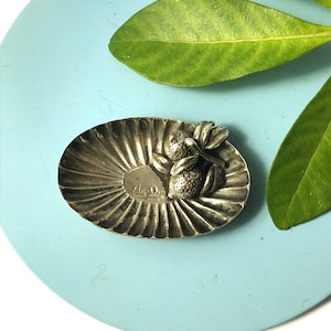May include: A silver dish with a scalloped edge and a raised design of three limes with leaves. The dish is marked "Ay-Oo" and "Italy".