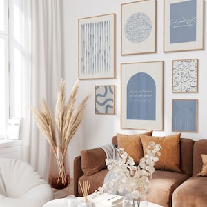 May include: A collection of framed wall art with blue and beige abstract designs and calligraphy. The art pieces are displayed above a brown sofa with orange pillows. A large vase with dried pampas grass and a white coffee table complete the room's decor.